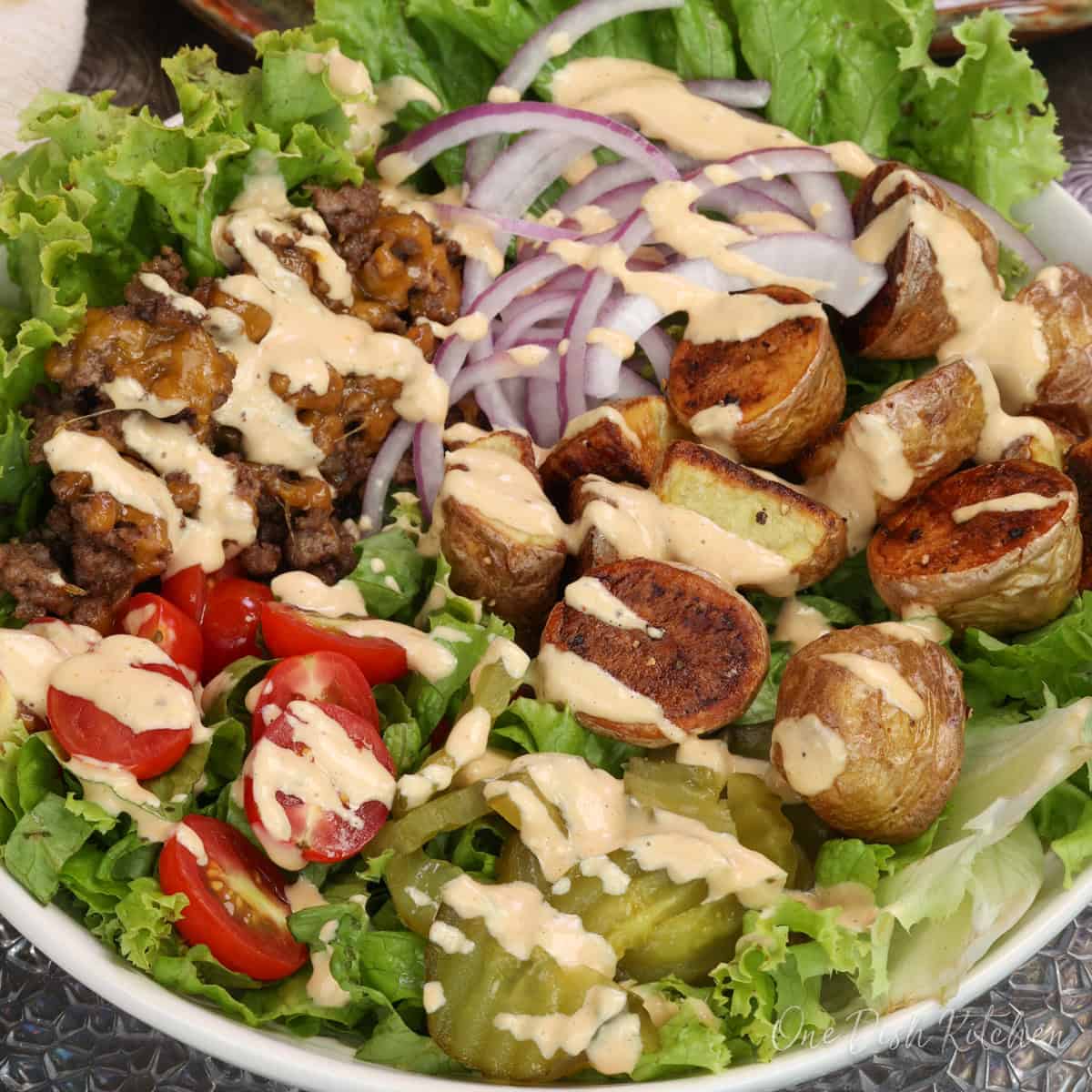 a burger bowl with ground beef, lettuce, tomatoes, pickles, onions, beef and cheese.