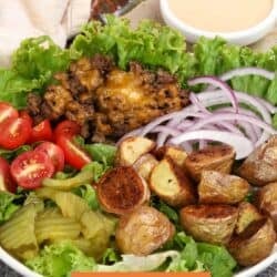 a burger bowl on a silver tray with a bowl of burger sauce on the side.