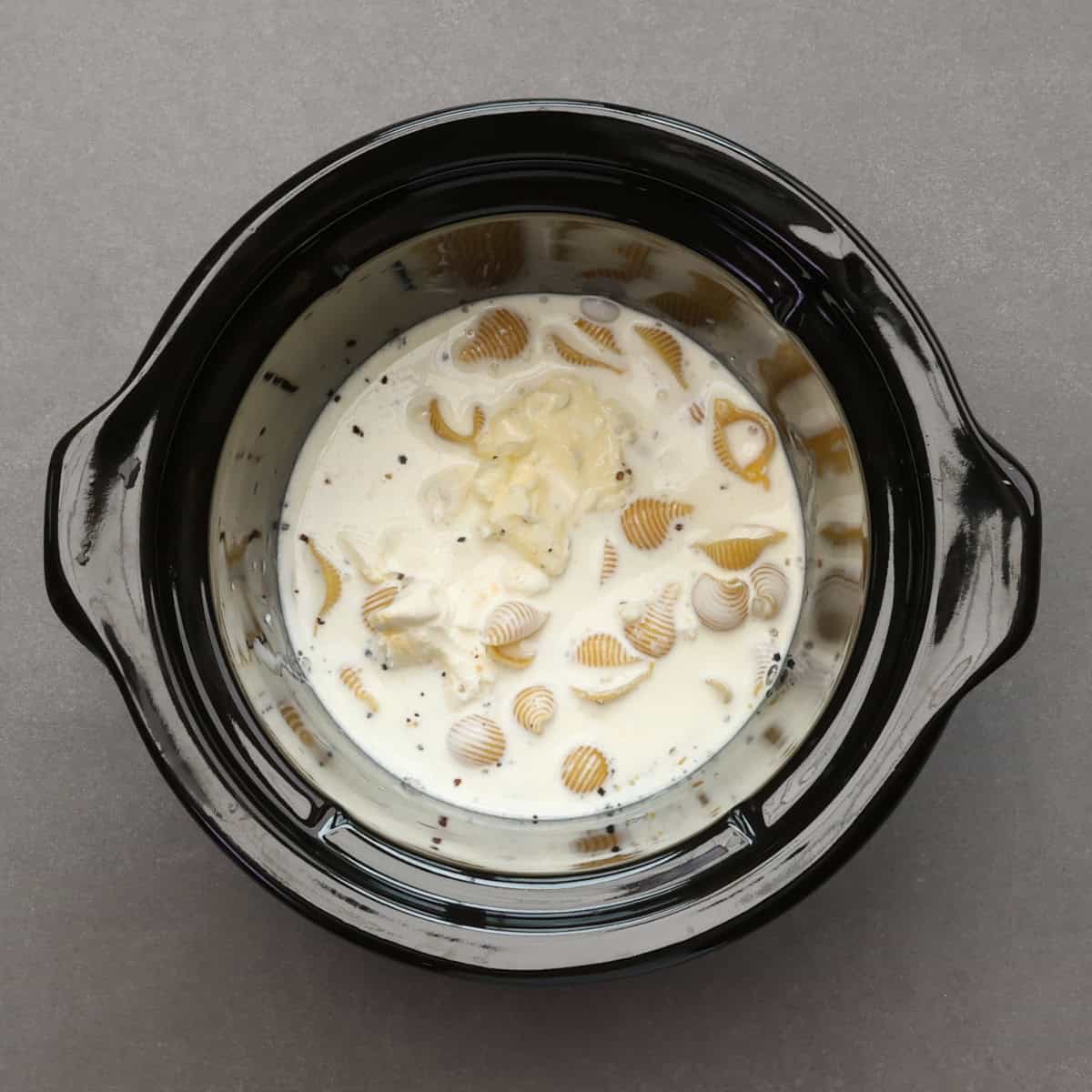 uncooked pasta, cream, milk, butter, and cream cheese in the base of a small crockpot.
