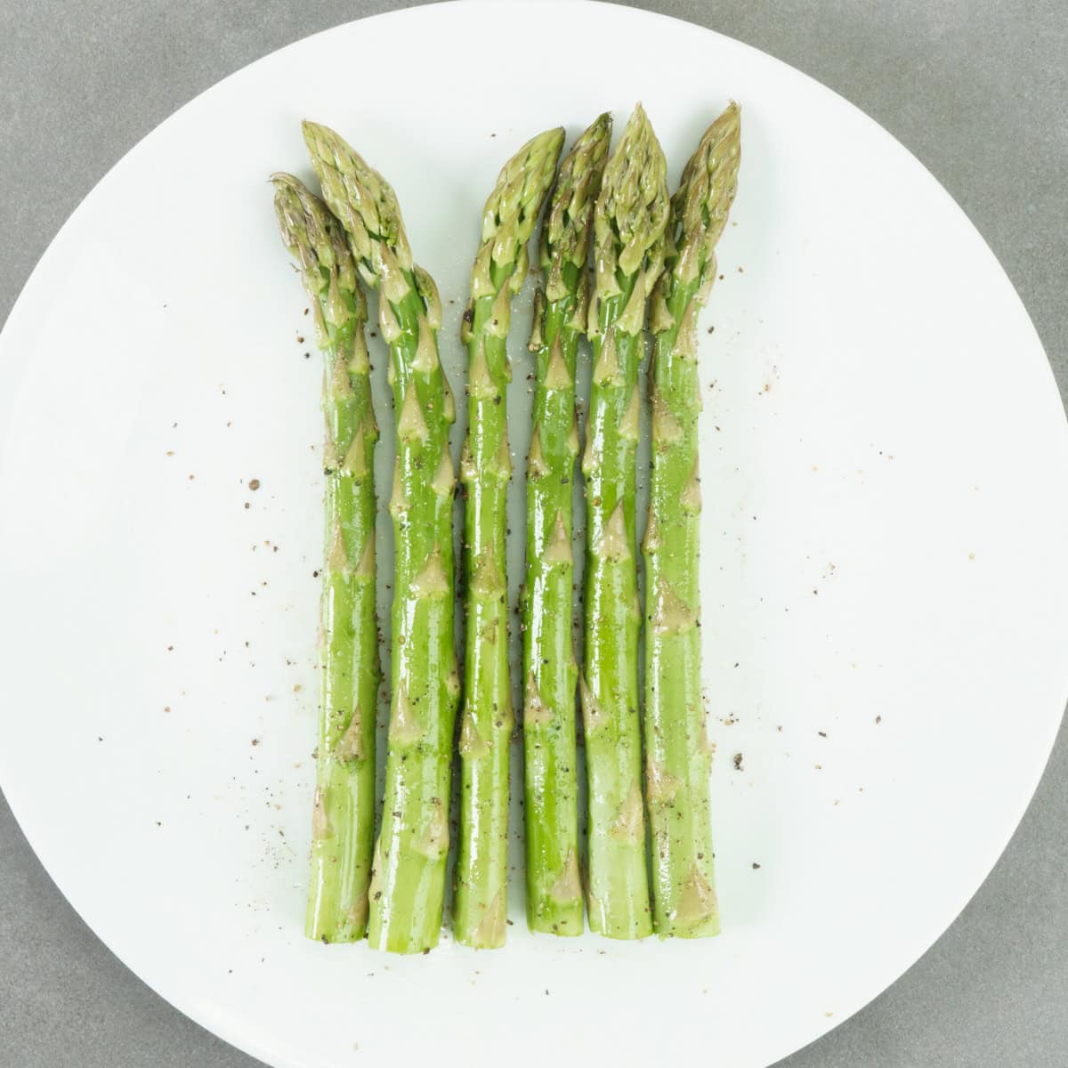 six fresh asparagus spears on a white plate.