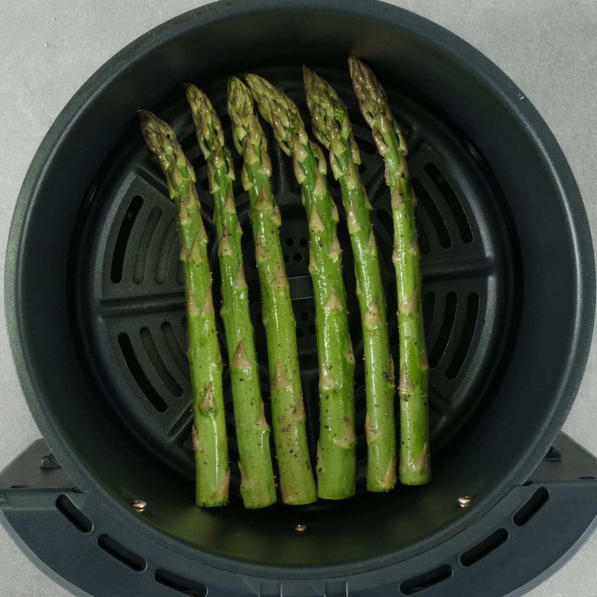 seasoned asparagus in an air fryer basket.