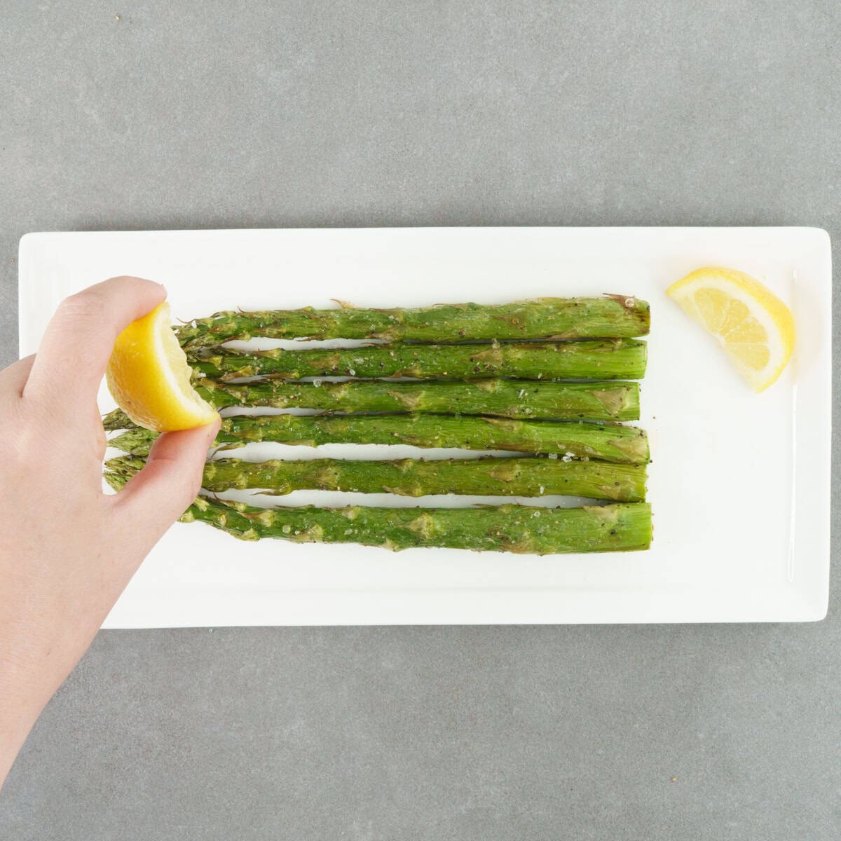 cooked asparagus on a plate with lemon wedges on the side.