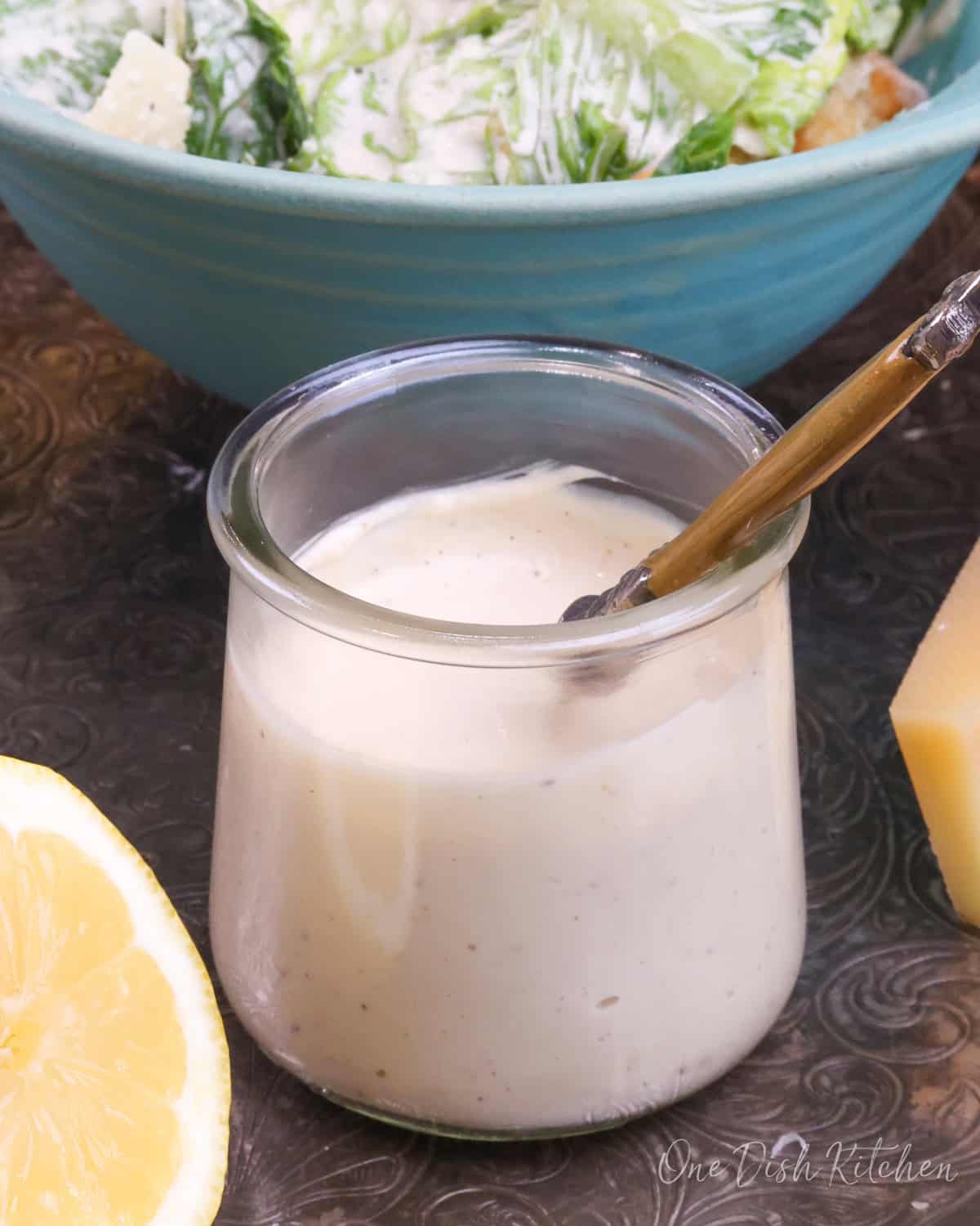 a small jar of caesar salad dressing next to a caesar salad.