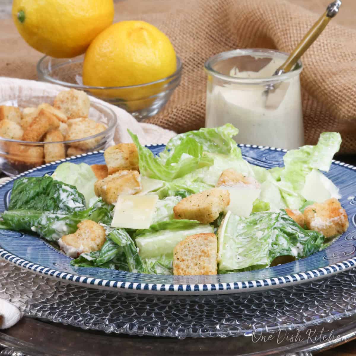 a caesar salad on a blue plate topped with caesar dressing, croutons, and parmesan cheese.