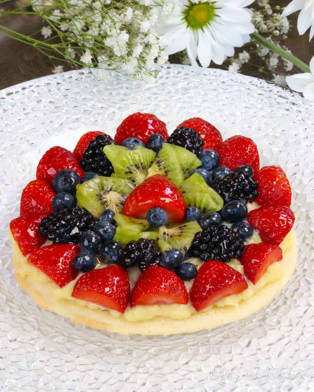 a small fruit tart topped with fresh fruit next to white flowers.