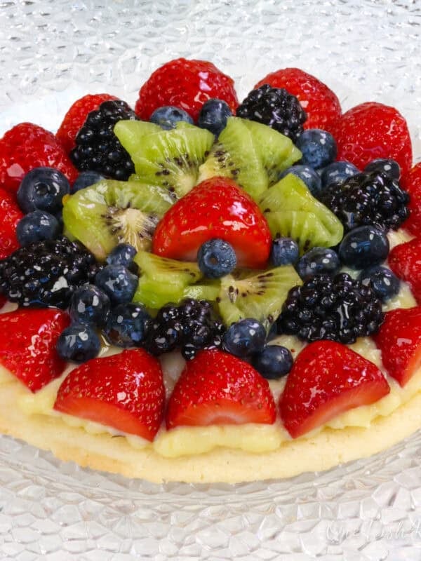 a small fruit tart topped with fresh fruit next to white flowers.