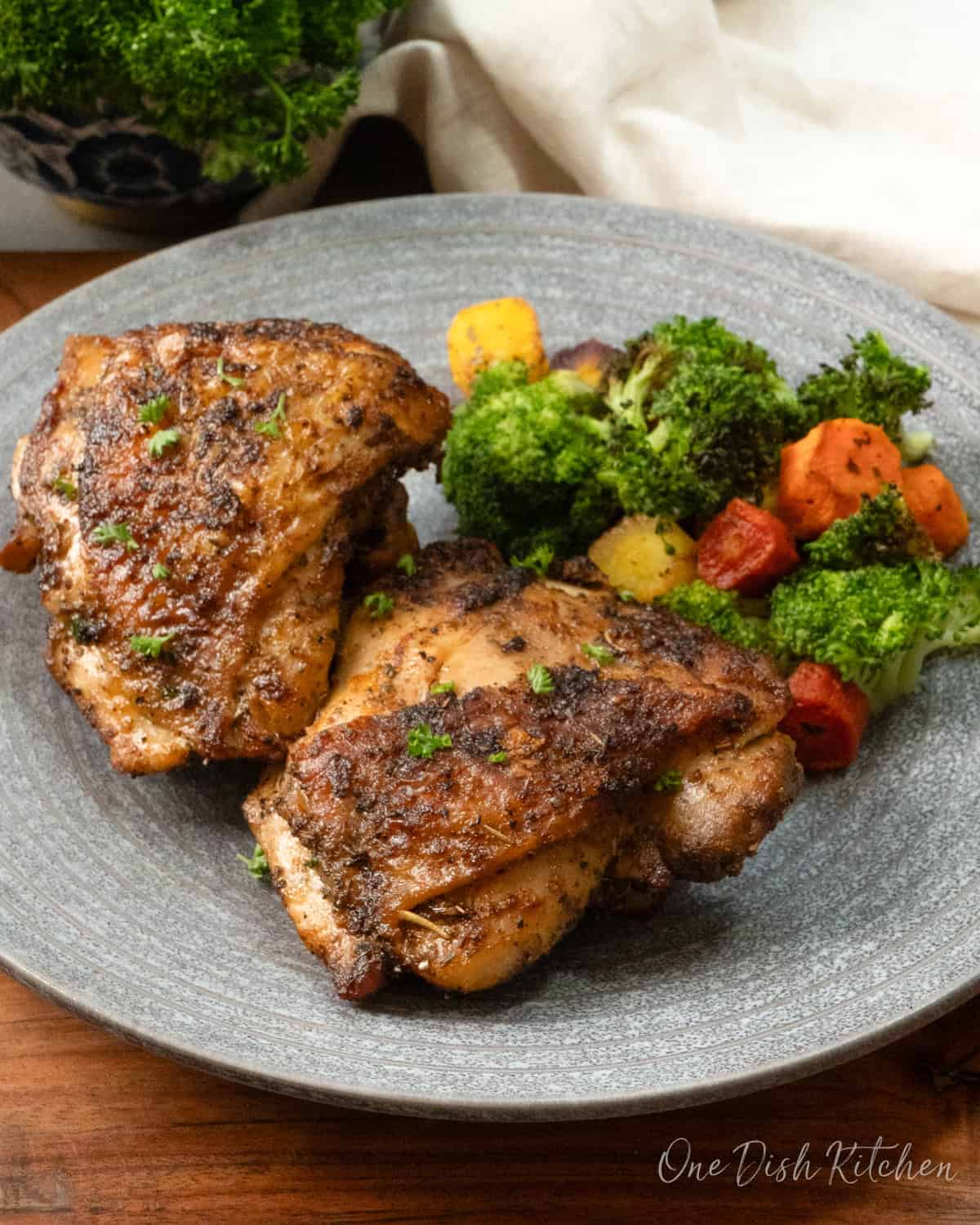 two air fryer chicken thighs on a plate with broccoli and carrots.