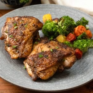 two air fryer chicken thighs on a plate with broccoli and carrots.
