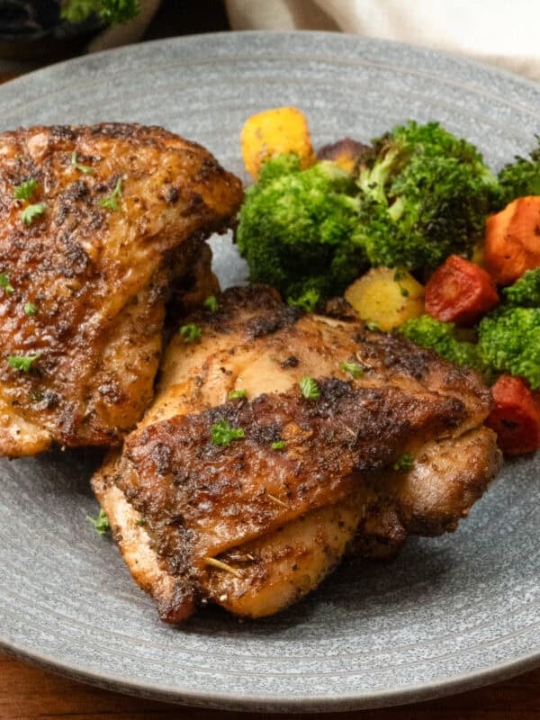 two air fryer chicken thighs on a plate with broccoli and carrots.