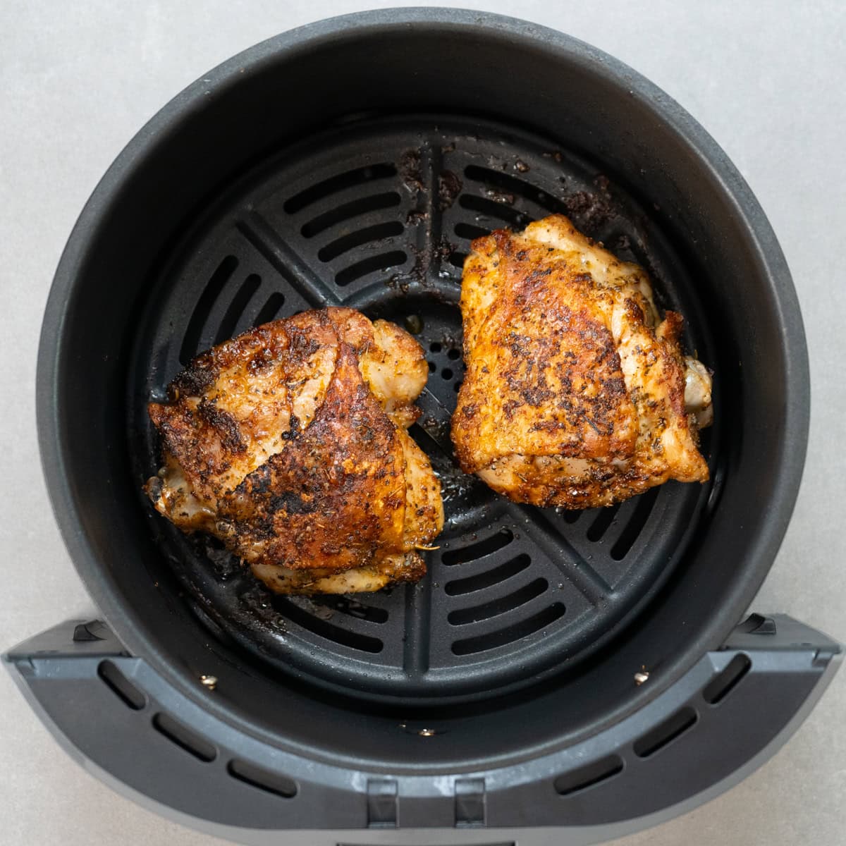 two cooked chicken thighs in an air fryer basket.