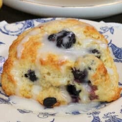 two blueberry scones on plates next to a yellow bowl of fresh blueberries.