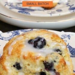 two blueberry scones on plates next to a yellow bowl of fresh blueberries.