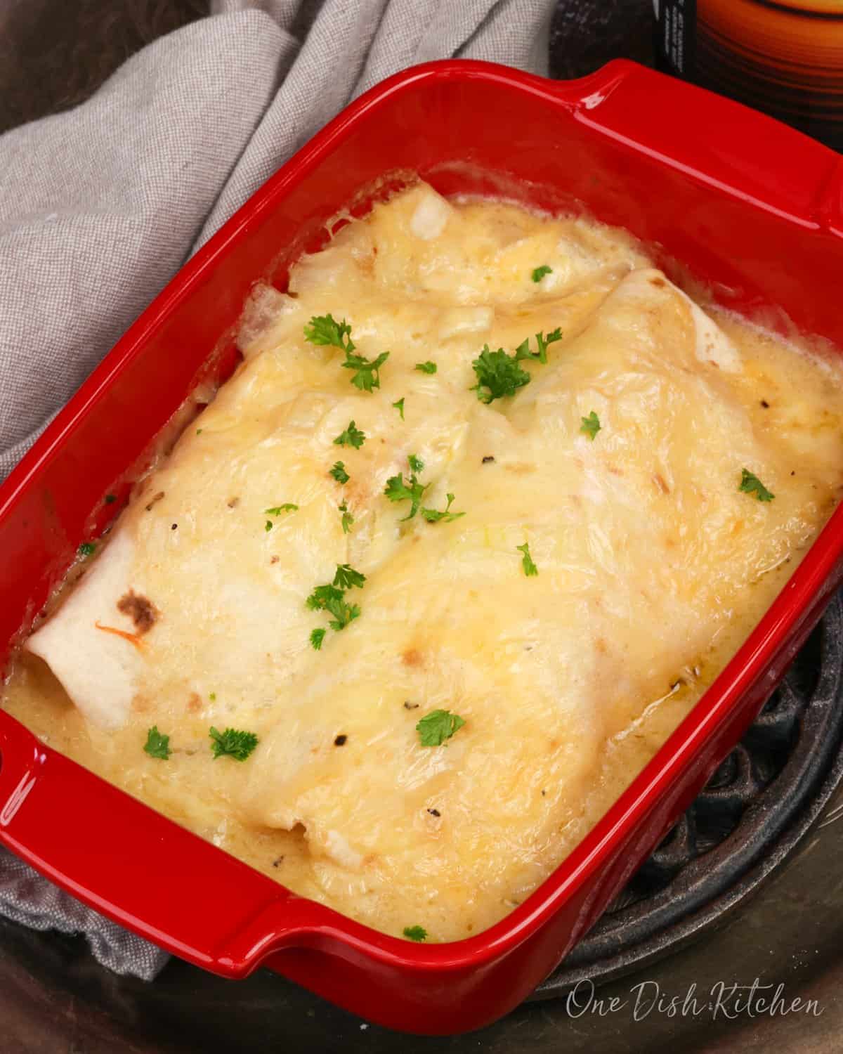 two chicken enchiladas in homemade sauce in a red baking dish.