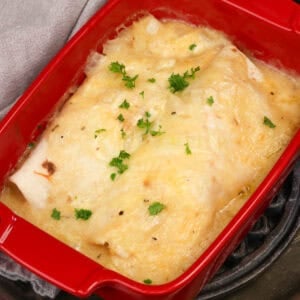 two chicken enchiladas in homemade sauce in a red baking dish.