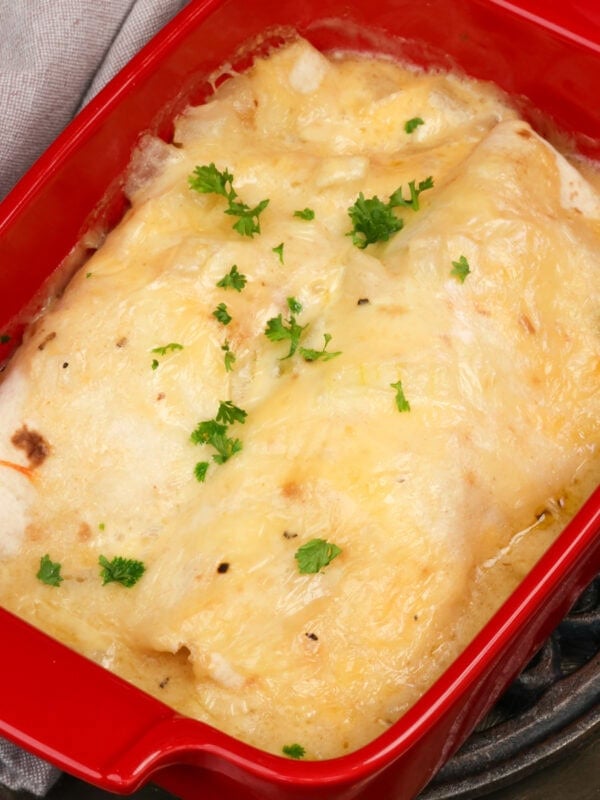 two chicken enchiladas in homemade sauce in a red baking dish.