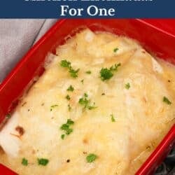 two chicken enchiladas in homemade sauce in a red baking dish.