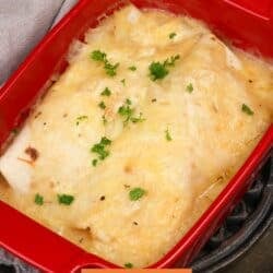 two chicken enchiladas in homemade sauce in a red baking dish.