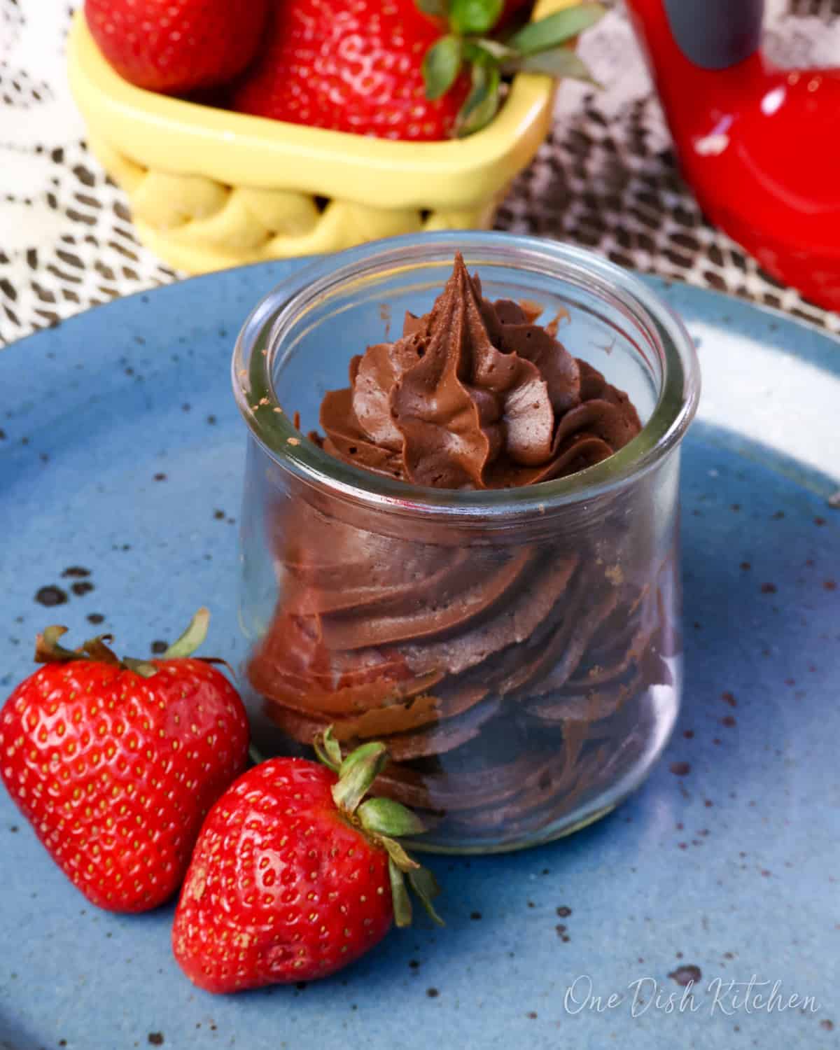 a small batch of chocolate frosting in a jar surrounded by fresh strawberries.