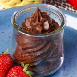 a small batch of chocolate frosting in a jar surrounded by fresh strawberries.
