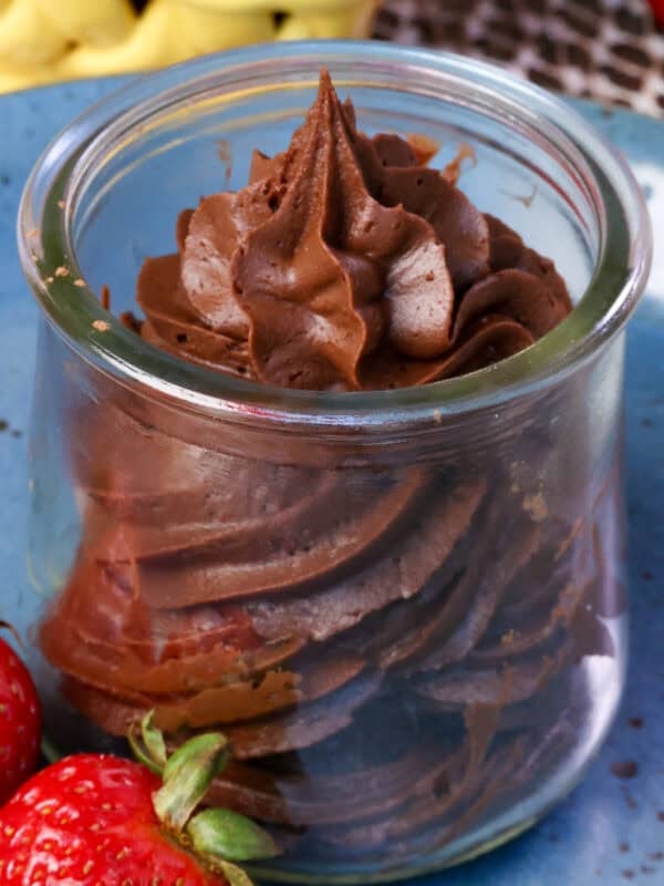 a small batch of chocolate frosting in a jar surrounded by fresh strawberries.