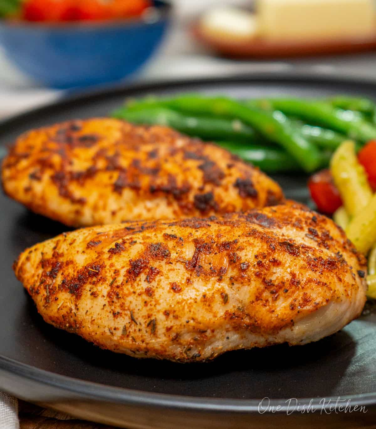 two air fryer chicken breasts on a black plate next to pasta and a salad.