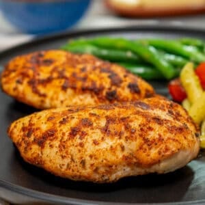two air fryer chicken breasts on a black plate next to pasta and a salad.