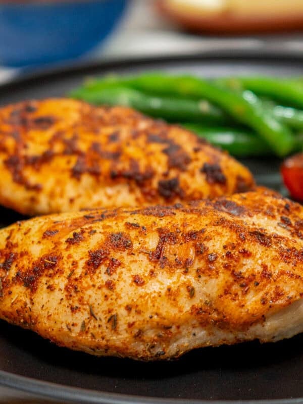 two air fryer chicken breasts on a black plate next to pasta and a salad.
