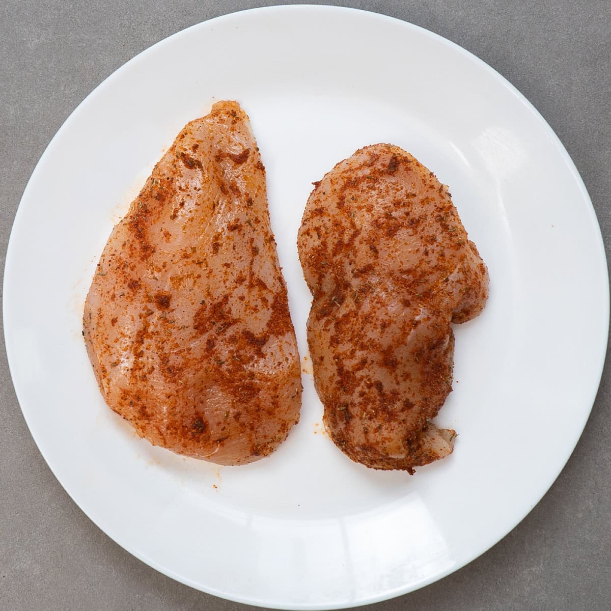 two seasoned chicken breasts on a white plate.