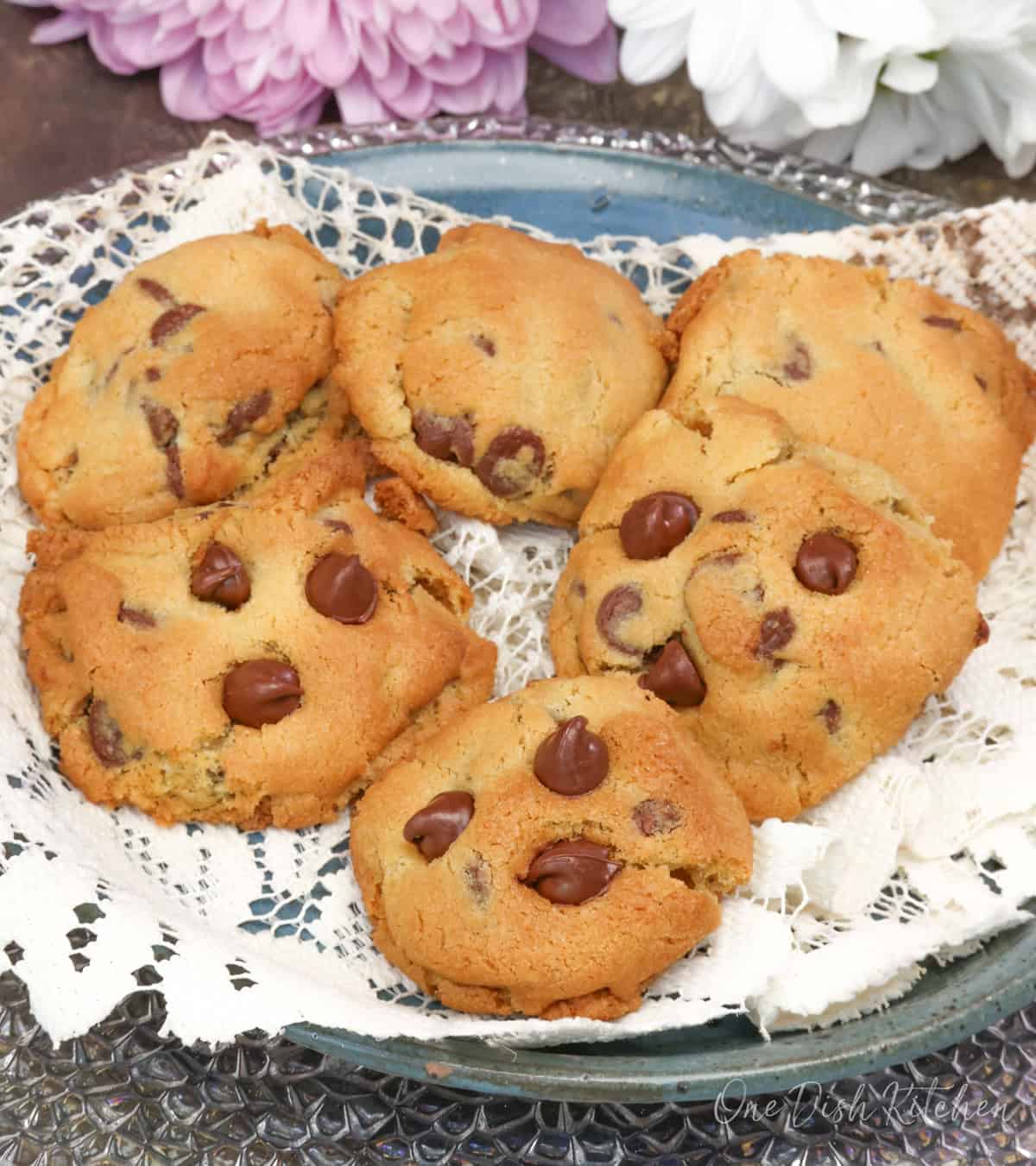 a plate of chocolate chip cookies next to fresh flowers.