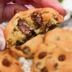 half a chocolate chip cookie in a hand next to cookies on a plate.