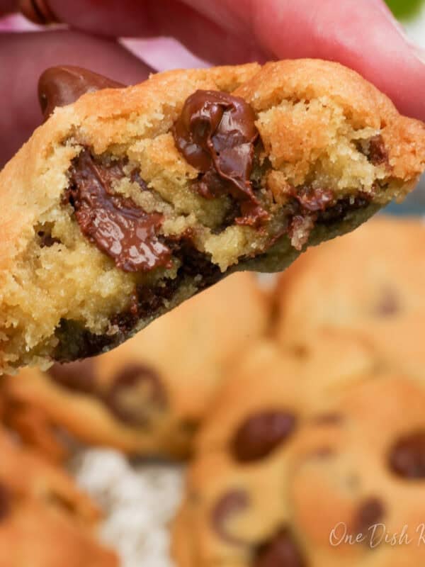 half a chocolate chip cookie in a hand next to cookies on a plate.