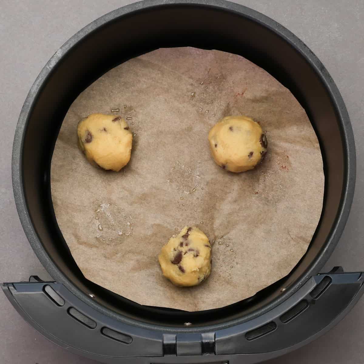 three unbaked chocolate chip cookies in an air fryer basket.