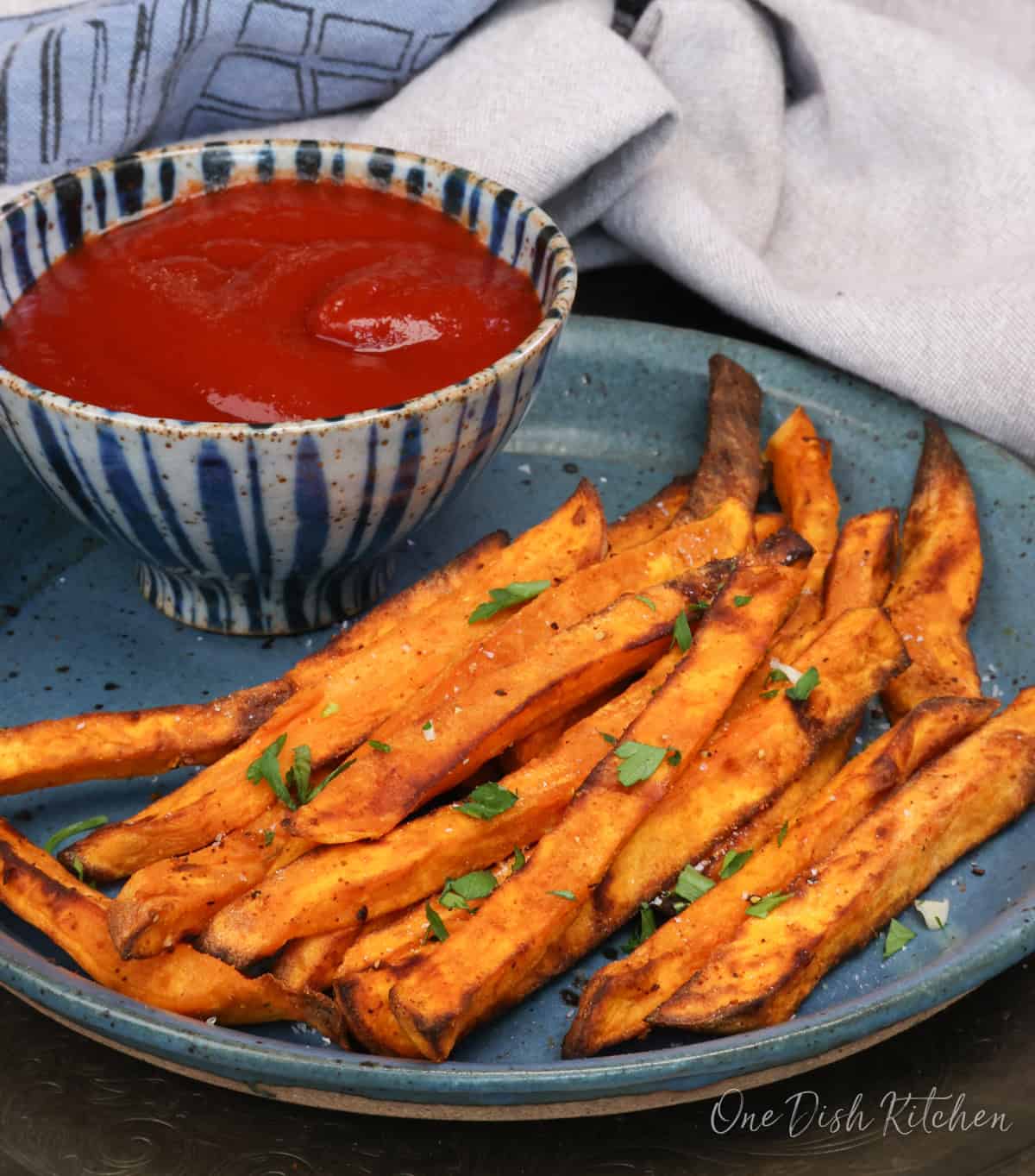 sweet potato fries on a blue plate next to a bowl of ketchup.