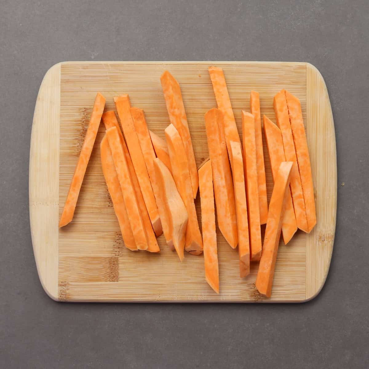 sliced sweet potato into fries on a cutting board.