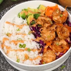 a bang bang shrimp rice bowl on a white plate next to a jar of bang bang sauce.