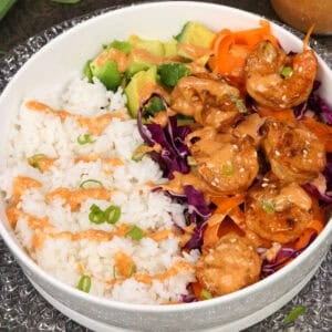 a bang bang shrimp rice bowl on a white plate next to a jar of bang bang sauce.