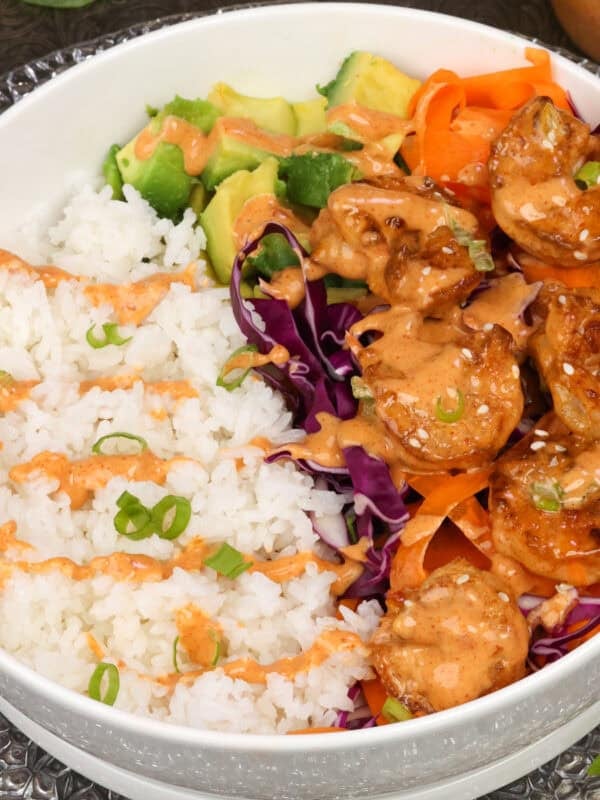 a bang bang shrimp rice bowl on a white plate next to a jar of bang bang sauce.