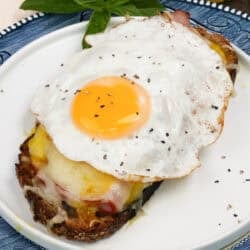 an open faced croque madame on a white plate next to fresh basil.