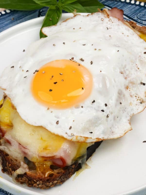an open faced croque madame on a white plate next to fresh basil.