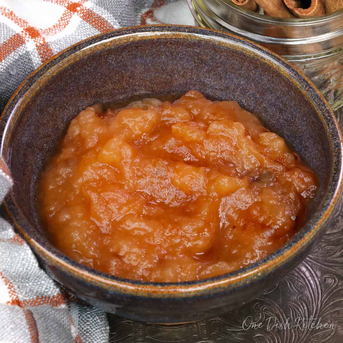 applesauce in a bowl next to a jar of cinnamon sticks.