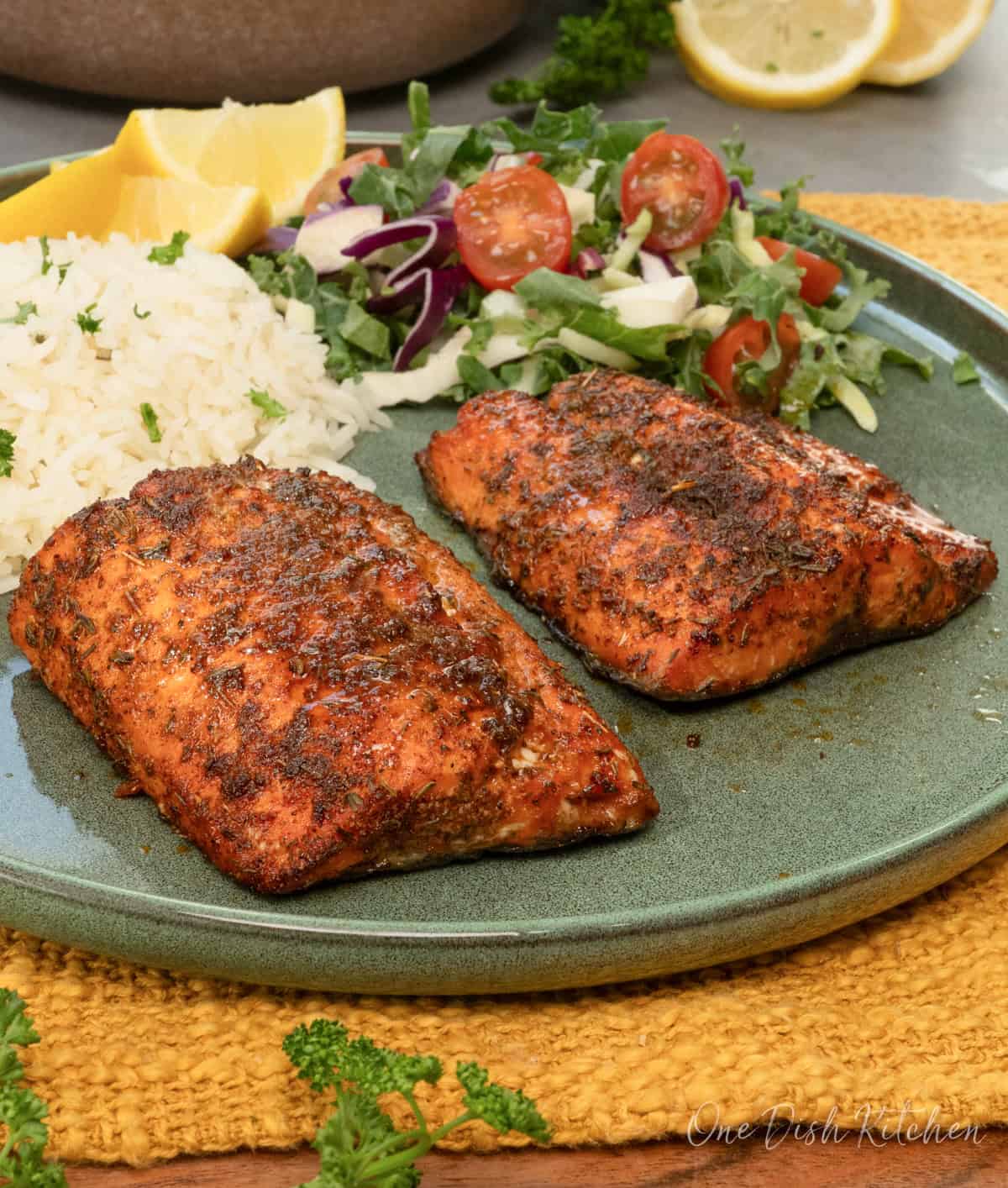 two air fryer salmon fillets on a green plate next to rice and a salad.