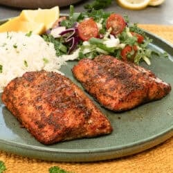 two air fryer salmon fillets on a green plate next to rice and a salad.