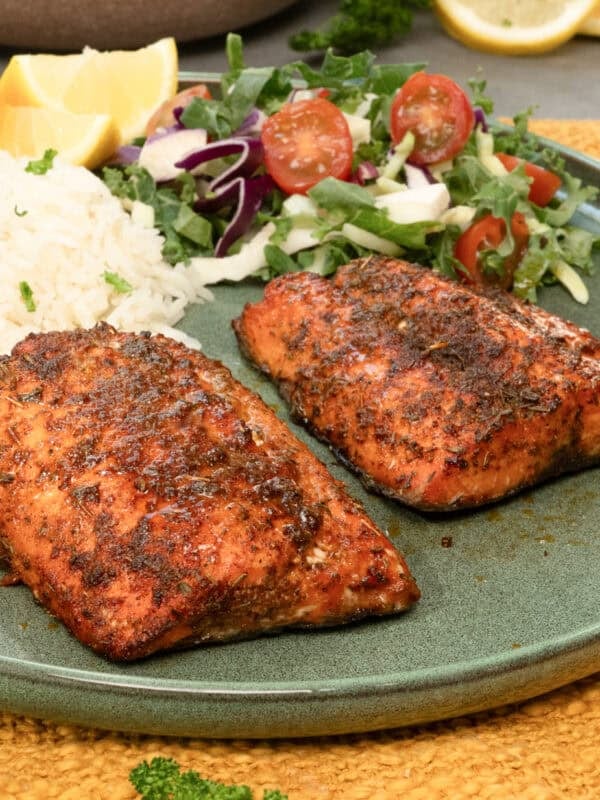two air fryer salmon fillets on a green plate next to rice and a salad.