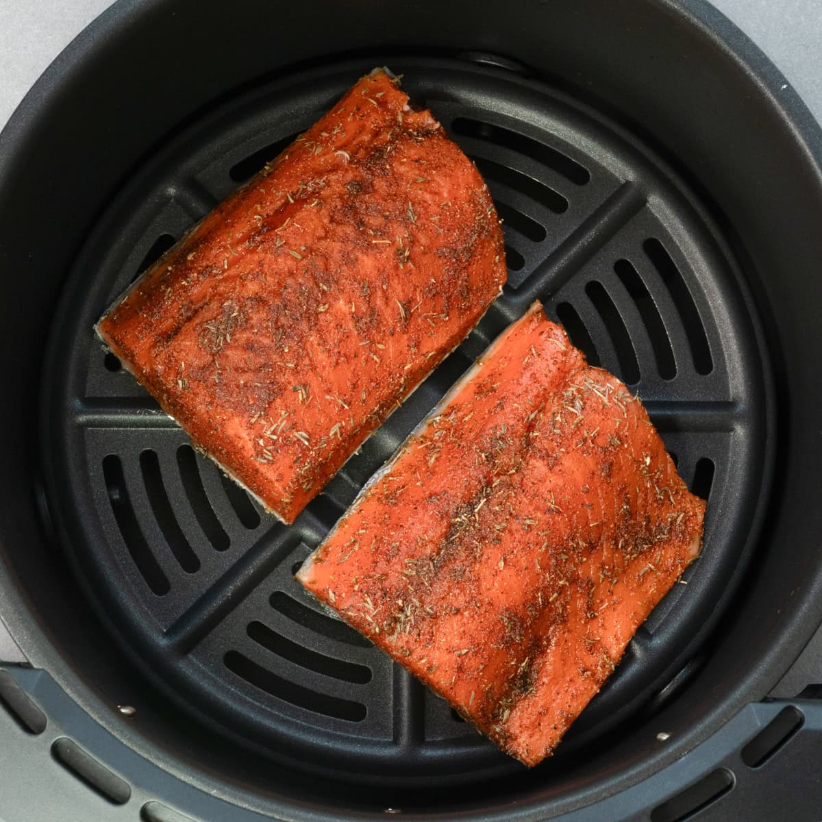 two salmon fillets in an air fryer basket.