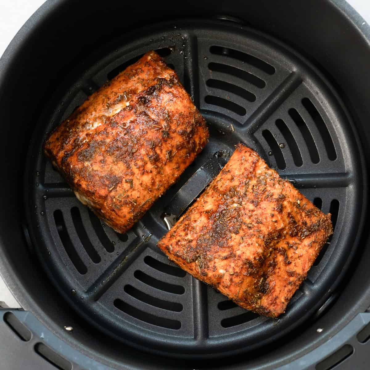 two cooked salmon fillets in an air fryer basket.