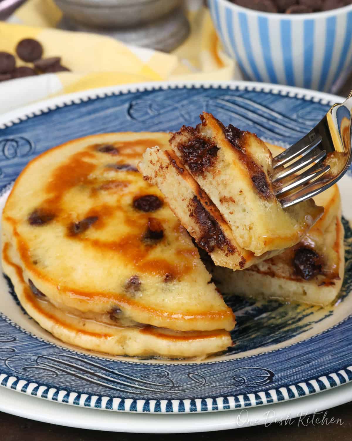 two chocolate chip pancakes on a blue plate with a fork on the side.