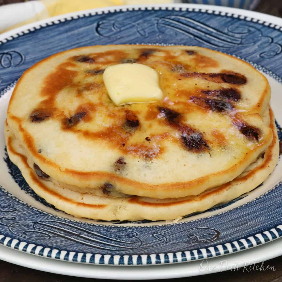 two chocolate chip pancakes on a blue plate topped with butter.