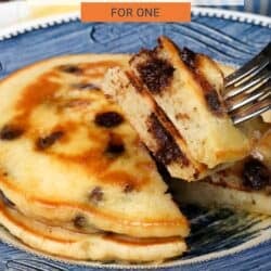 two fluffy chocolate chip pancakes on a blue plate with a fork on the side.