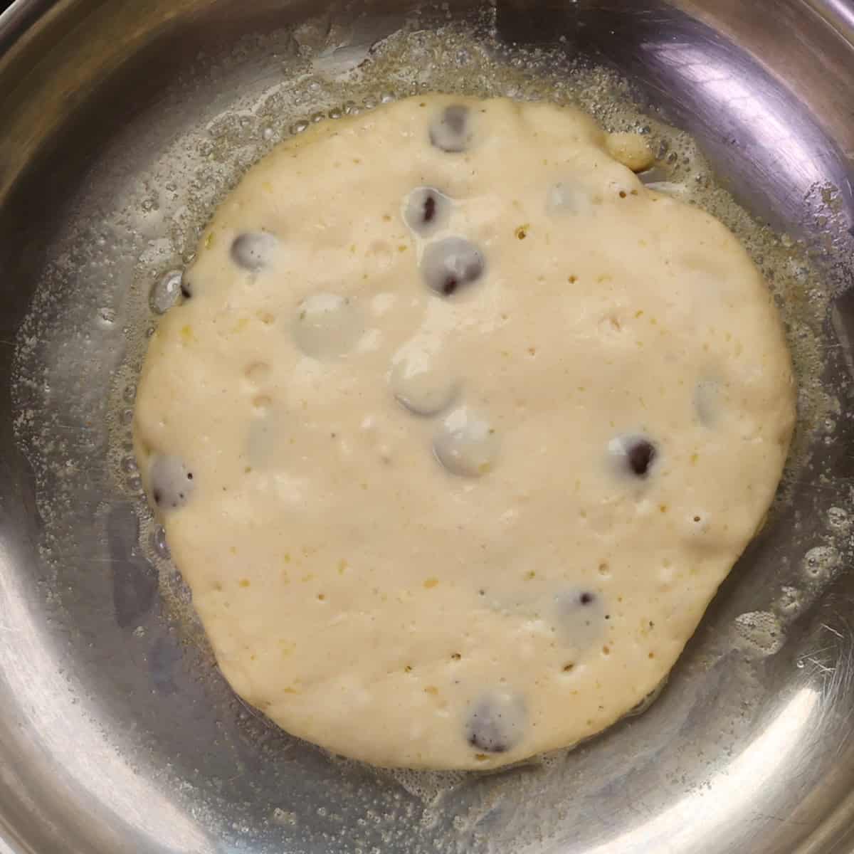 one chocolate chip pancakes cooking in a skillet.