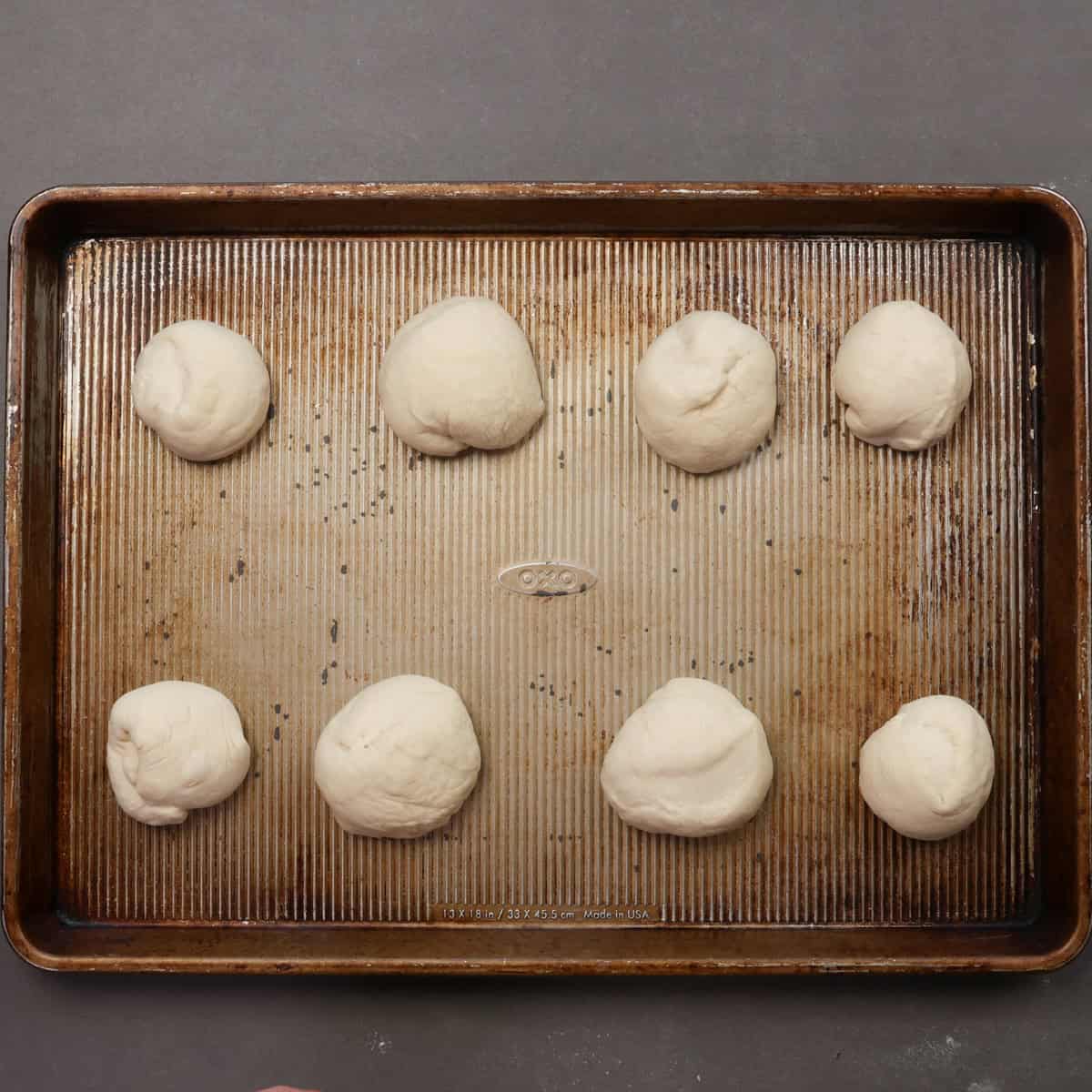 eight unbaked dinner rolls on a baking sheet.